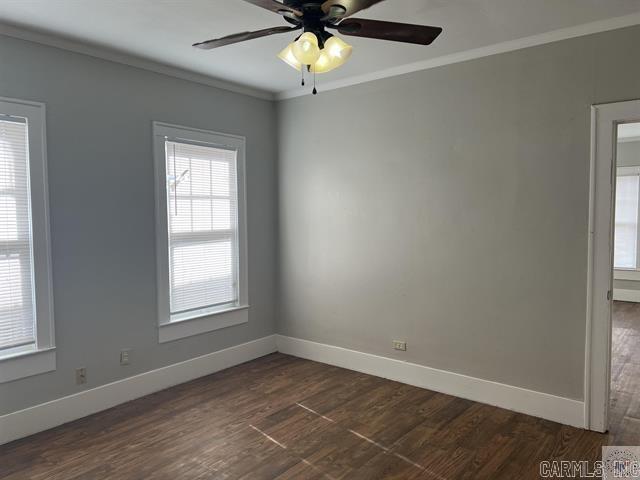 empty room featuring dark wood-style floors, baseboards, a ceiling fan, and crown molding