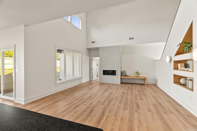 unfurnished living room featuring light wood-type flooring, a large fireplace, visible vents, and baseboards