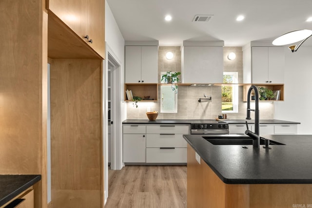 kitchen featuring visible vents, dark countertops, backsplash, light wood-type flooring, and a sink