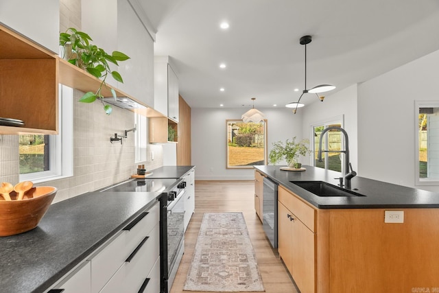 kitchen featuring electric range, dark countertops, an island with sink, a sink, and stainless steel dishwasher