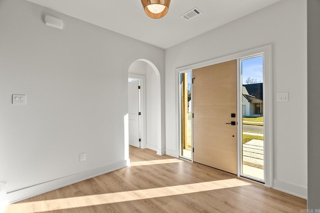 foyer entrance featuring arched walkways, visible vents, baseboards, and wood finished floors