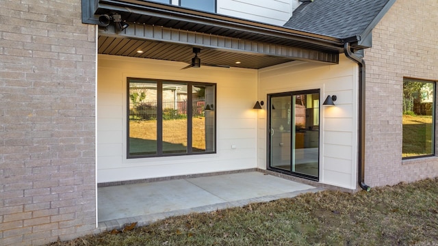 entrance to property featuring brick siding, ceiling fan, a patio, and roof with shingles