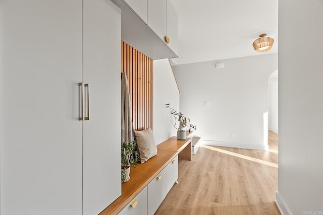 mudroom featuring light wood-type flooring, baseboards, and arched walkways