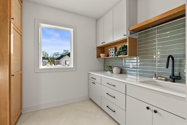 interior space with baseboards, decorative backsplash, light countertops, open shelves, and a sink