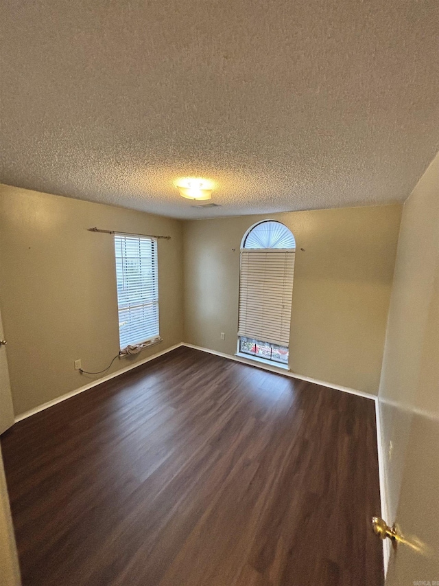 unfurnished room with dark wood-style floors, a textured ceiling, and baseboards