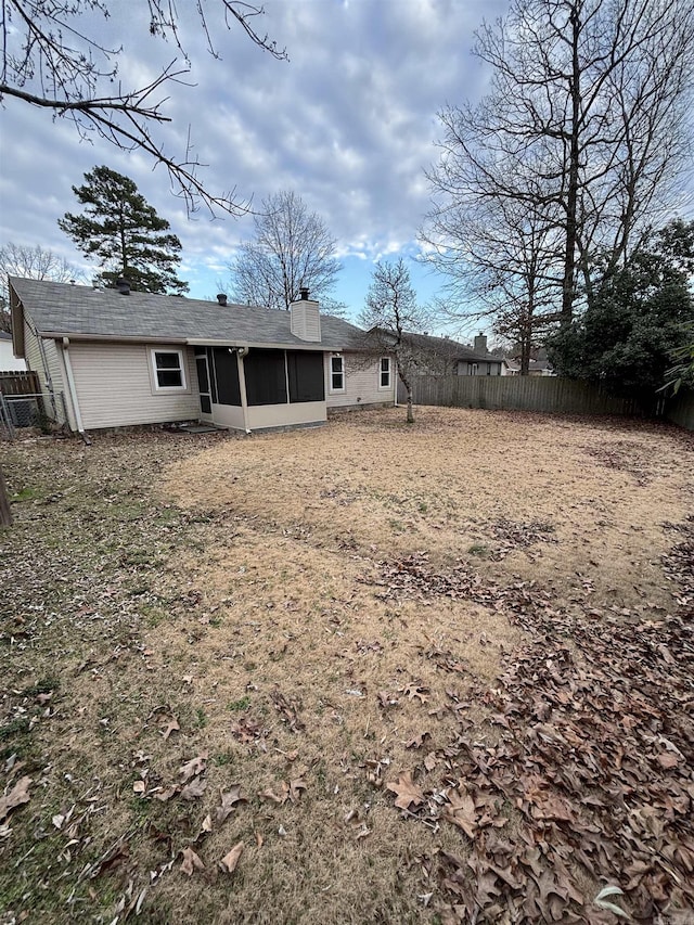 rear view of house featuring a chimney, fence, and a sunroom