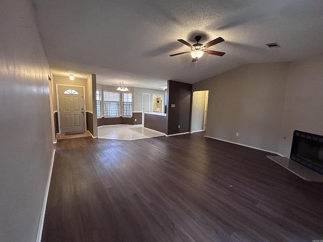 unfurnished living room featuring visible vents, a fireplace with raised hearth, dark wood-style floors, a textured ceiling, and ceiling fan with notable chandelier