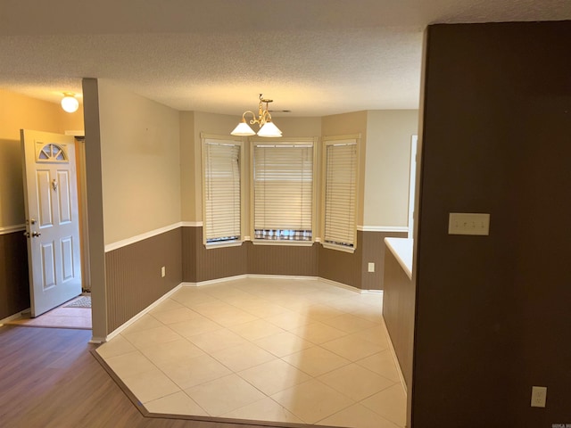 empty room with a chandelier, wainscoting, and a textured ceiling