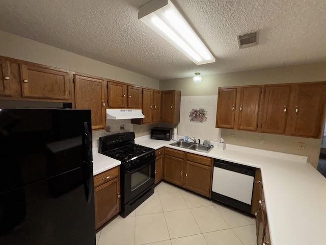 kitchen featuring black appliances, under cabinet range hood, brown cabinetry, and a sink