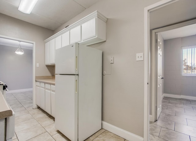 kitchen featuring light tile patterned floors, baseboards, white cabinets, light countertops, and freestanding refrigerator