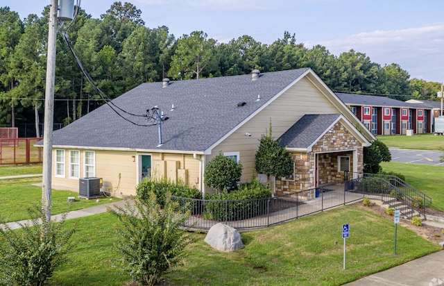 view of front of house with central air condition unit, fence, a front lawn, and roof with shingles
