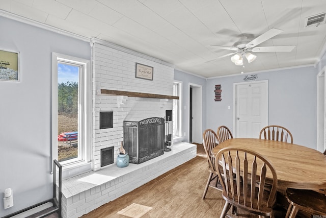 dining area featuring visible vents, a ceiling fan, wood finished floors, crown molding, and a fireplace