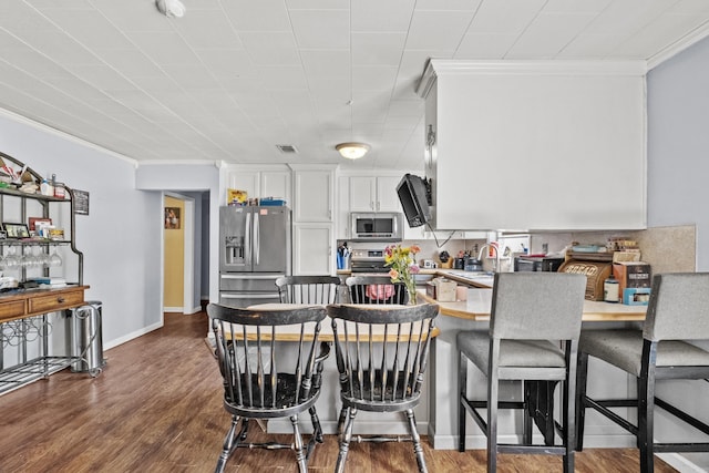 kitchen featuring stainless steel appliances, a peninsula, dark wood finished floors, ornamental molding, and a kitchen bar