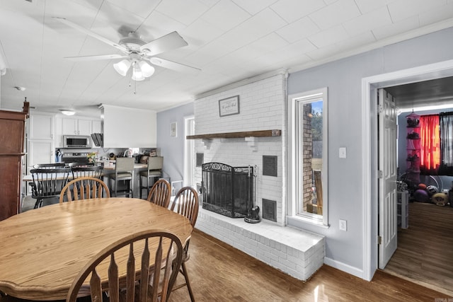 dining room with a fireplace, baseboards, wood finished floors, and ornamental molding