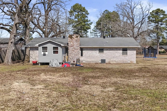 rear view of house with central AC unit, a trampoline, brick siding, crawl space, and a chimney