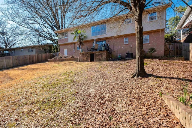 rear view of house featuring a yard, brick siding, fence, and central AC