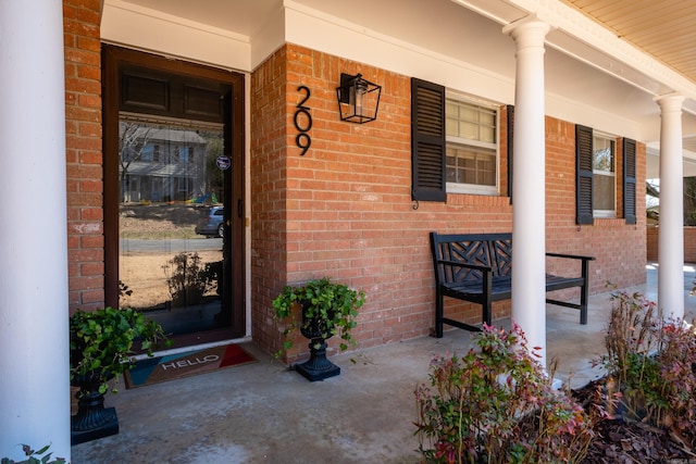 doorway to property with covered porch and brick siding