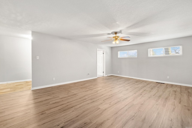 spare room featuring light wood-style floors, a textured ceiling, and baseboards