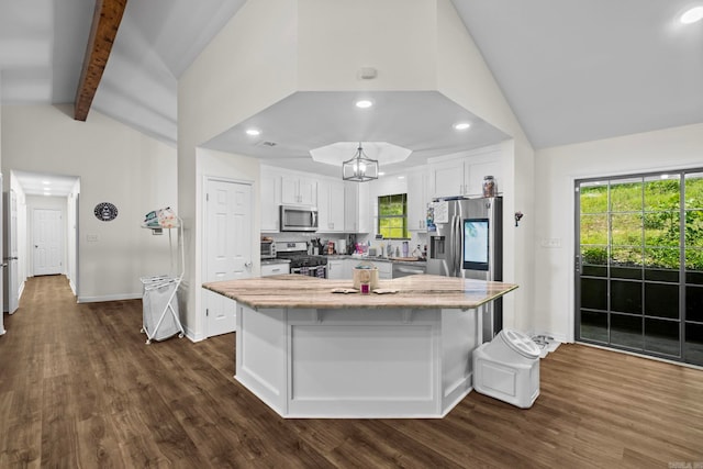 kitchen featuring vaulted ceiling with beams, light stone counters, stainless steel appliances, white cabinetry, and a center island