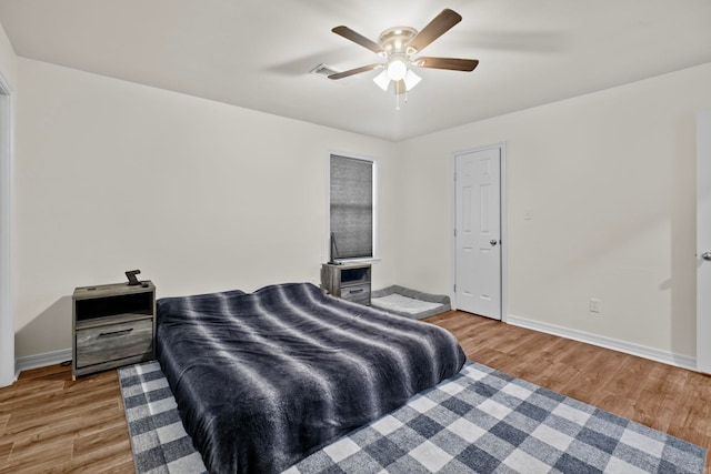 bedroom with a ceiling fan, visible vents, baseboards, and wood finished floors