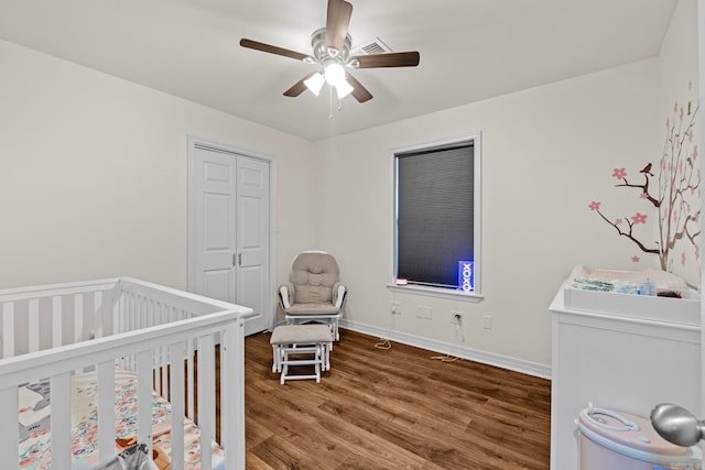 bedroom featuring wood finished floors, a ceiling fan, baseboards, a closet, and a crib