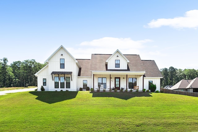 modern farmhouse featuring covered porch, board and batten siding, a front yard, and fence