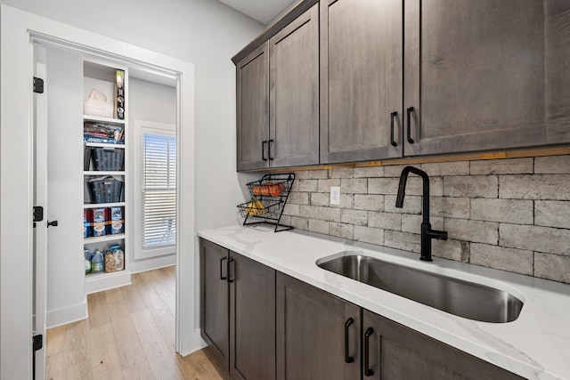 kitchen featuring light stone counters, a sink, backsplash, and dark brown cabinets