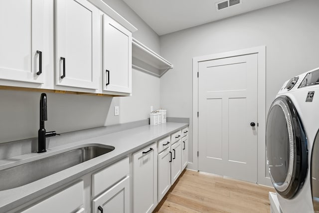 clothes washing area with cabinet space, visible vents, washer and clothes dryer, light wood-type flooring, and a sink