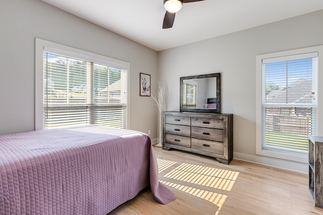 bedroom with light wood-style floors, multiple windows, baseboards, and a ceiling fan