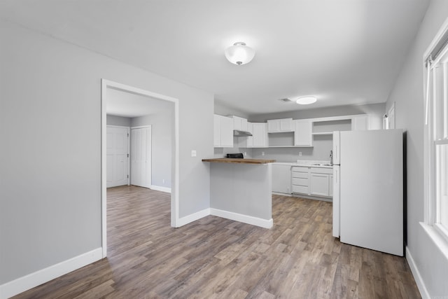 kitchen with baseboards, dark wood-type flooring, freestanding refrigerator, a peninsula, and under cabinet range hood