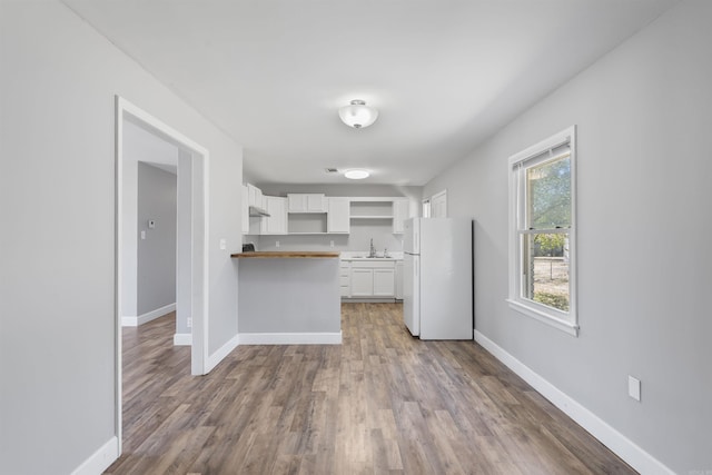 kitchen with freestanding refrigerator, white cabinets, a peninsula, and baseboards