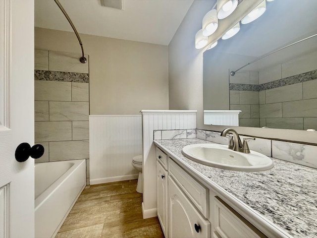 full bath featuring wainscoting, toilet, wood finished floors, vanity, and washtub / shower combination