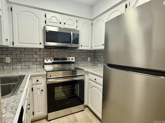 kitchen featuring tasteful backsplash, white cabinetry, stainless steel appliances, and light countertops