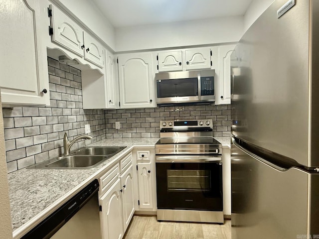 kitchen with light countertops, backsplash, appliances with stainless steel finishes, white cabinetry, and a sink