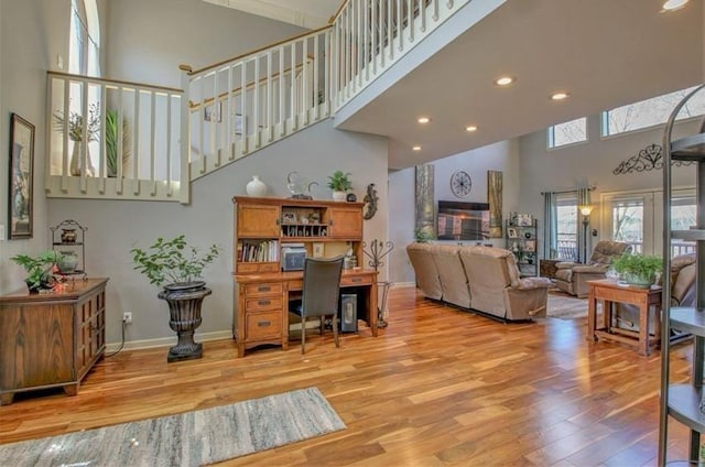 living area featuring a towering ceiling, light wood-style flooring, baseboards, and recessed lighting