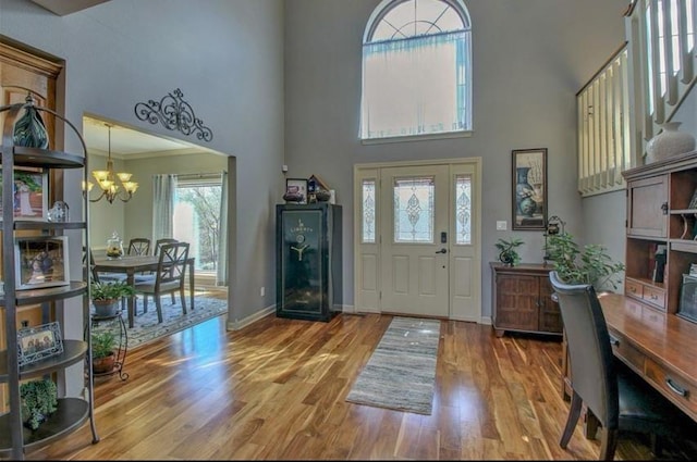 entryway with a chandelier, a towering ceiling, baseboards, and wood finished floors