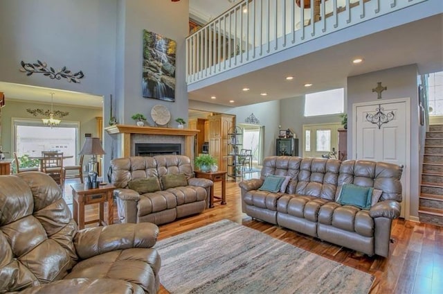 living area featuring wood finished floors, stairs, a high ceiling, a fireplace, and a notable chandelier