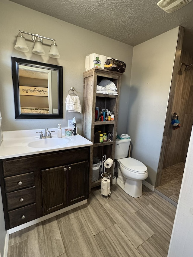 full bath with visible vents, toilet, wood finished floors, a tile shower, and a textured ceiling