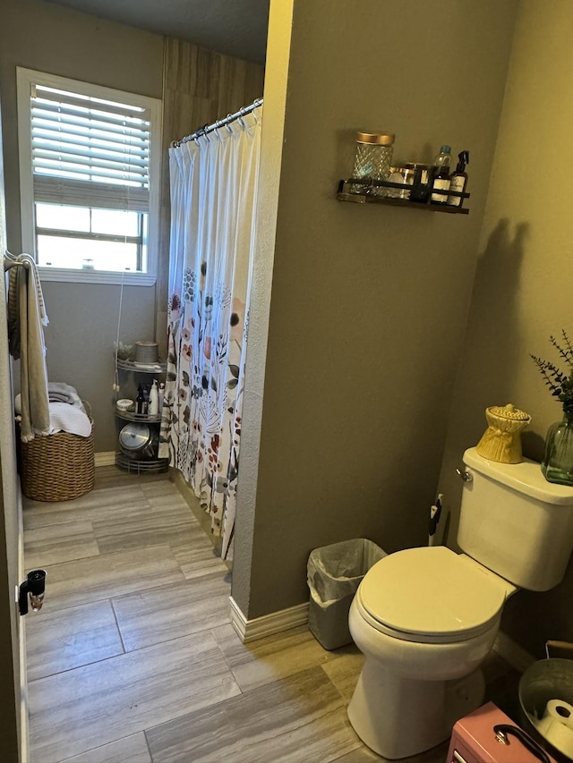 full bath with curtained shower, wood finished floors, toilet, and baseboards