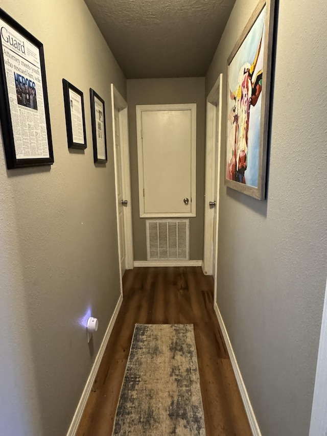 corridor with a textured ceiling, dark wood-style flooring, visible vents, and baseboards