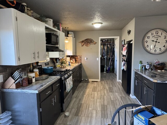 kitchen featuring under cabinet range hood, light countertops, a textured ceiling, black appliances, and white cabinetry