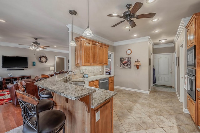 kitchen with a breakfast bar area, appliances with stainless steel finishes, a peninsula, light stone countertops, and a sink