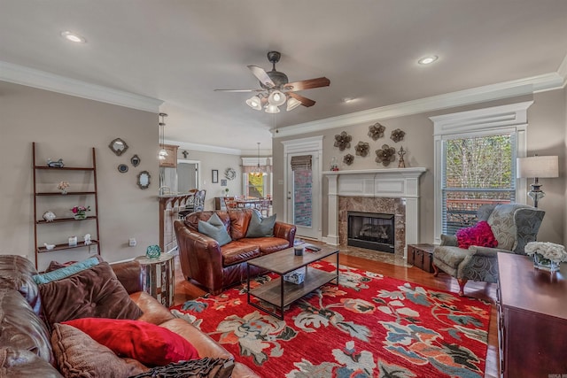 living area featuring a ceiling fan, a premium fireplace, ornamental molding, wood finished floors, and recessed lighting