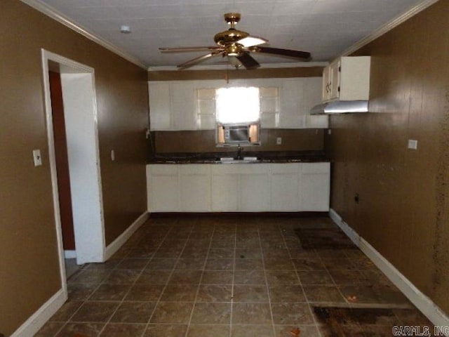 kitchen featuring dark countertops, ornamental molding, a ceiling fan, white cabinets, and a sink