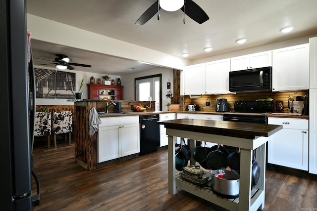 kitchen featuring butcher block counters, dark wood-type flooring, a peninsula, black appliances, and a sink