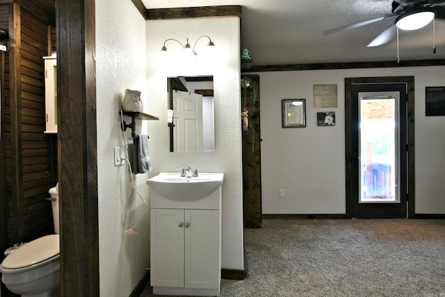 bathroom with ceiling fan, a textured wall, toilet, vanity, and baseboards