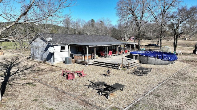 back of house with a deck, an outdoor fire pit, central AC unit, a pool, and roof with shingles