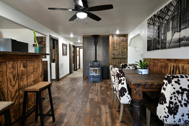 dining area with a textured ceiling, ceiling fan, dark wood-type flooring, and a wood stove