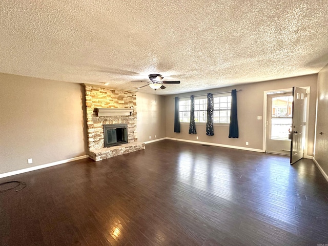 unfurnished living room featuring ceiling fan, a stone fireplace, dark wood-style flooring, and baseboards