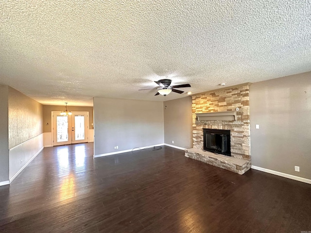 unfurnished living room with a textured ceiling, ceiling fan with notable chandelier, a fireplace, baseboards, and dark wood-style floors